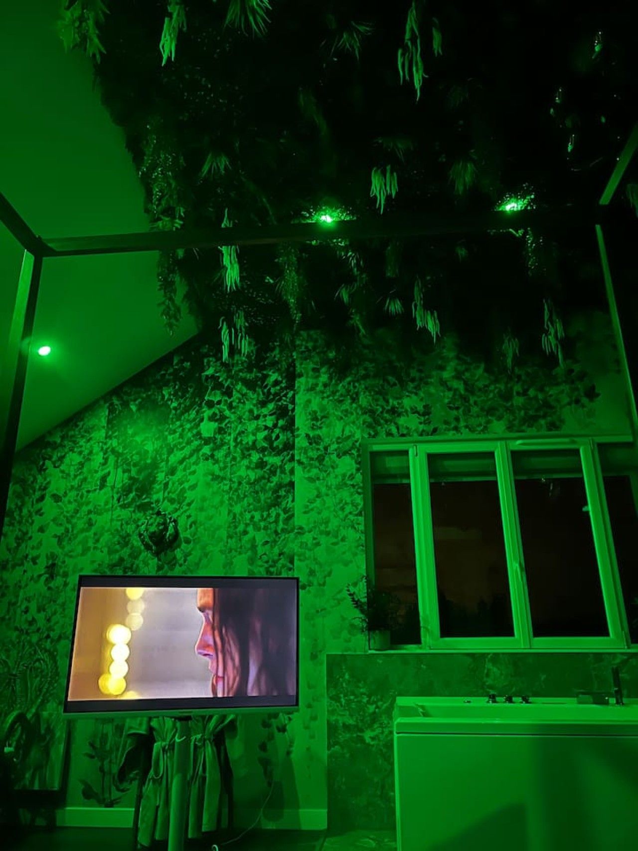 Ein Zimmer mit einer Wand in grünem Licht, einem Fernseher und einem Fenster.
