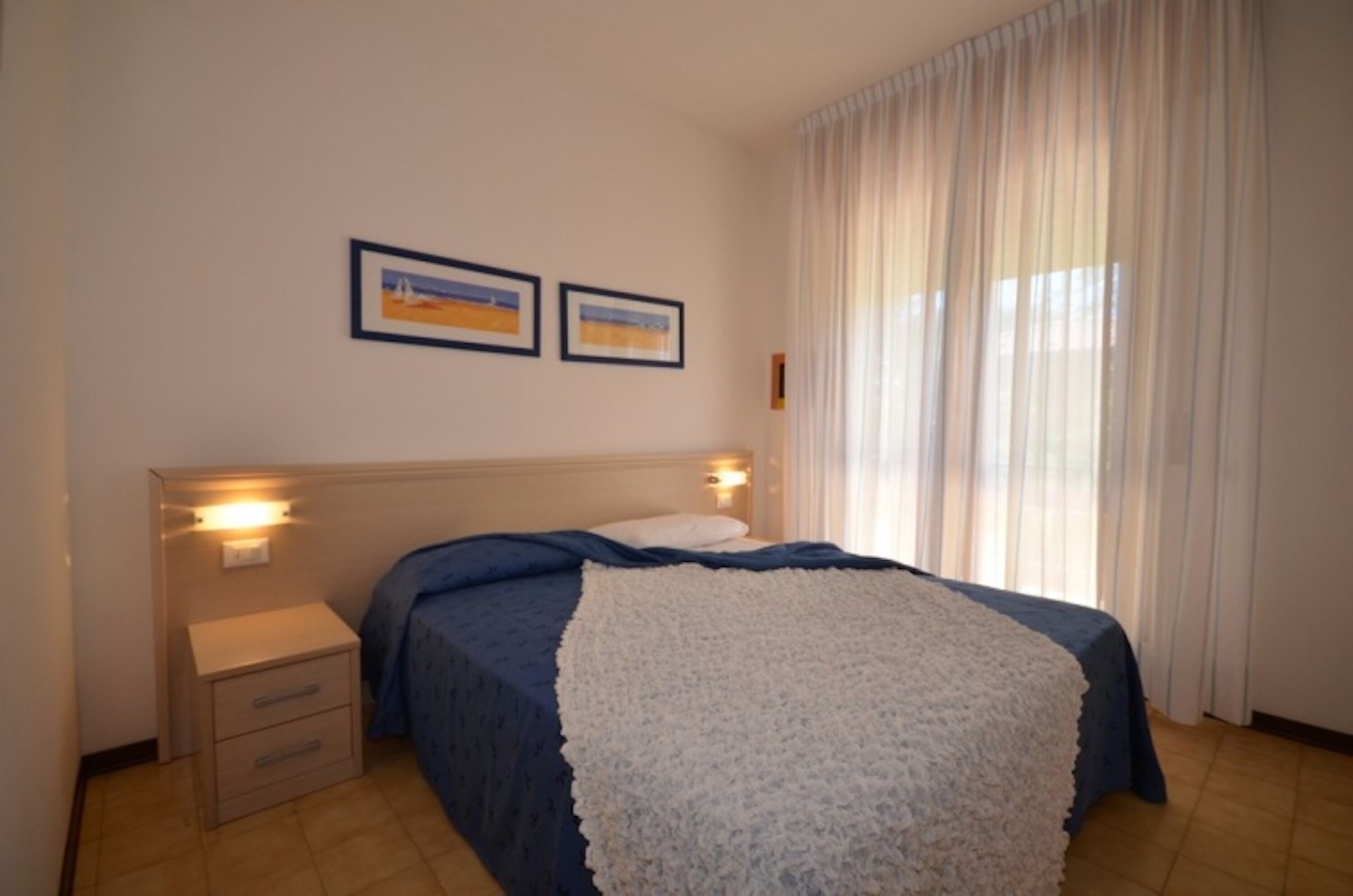 A bedroom with a bed, a nightstand, and two framed pictures on the wall.