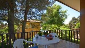 A balcony with a white table and chairs, surrounded by trees and a yellow building in the background. - Quiet holiday flat with pool (Bibione)