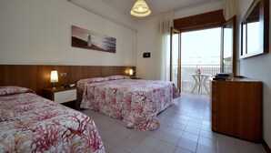 Ein Hotelzimmer mit zwei Betten, einem Schreibtisch, einem Sessel, einer Lampe, einem Gemälde und einem Balkon mit Blick.