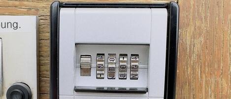 Näppäimistöllä varustettu sisäänpääsyjärjestelmä, jossa on metallinen pinta, säätönupilla varustettu ohjauspaneeli ja struktuuripinnoitettu seinä.