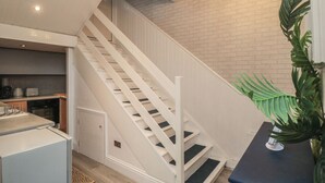 Un escalier avec des rampes blanches menant à un niveau supérieur, un coin cuisine équipé d’appareils modernes et un lustre.