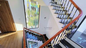 Eine moderne Treppe mit hölzernem Geländer und schwarzen Spindeln, die zu einem Balkon mit Blick auf Grünflächen führt.