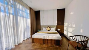 Ein modernes Hotelzimmer mit einem großen Bett, Holzboden und Blick ins Freie durch transparente Vorhänge.