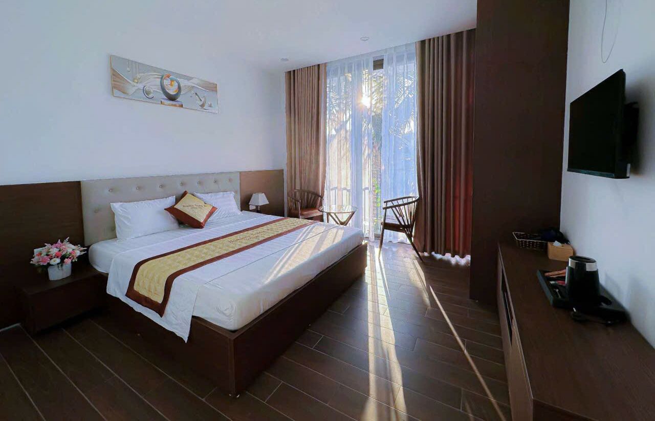 Quarto de hotel com uma cama grande, televisão de tela plana, uma mesa pequena e uma cadeira perto da janela.