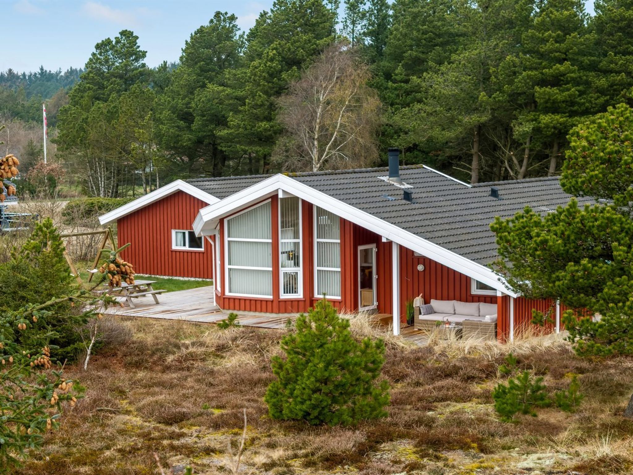 Een rode hut met een wit dak, omringd door bomen en een gazon.