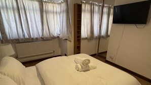 A hotel room with a bed, a radiator, a wardrobe, and a TV mounted on the wall. - Dagenham - Stay 5 - Garden - Parking - Petfriendly (Dagenham)