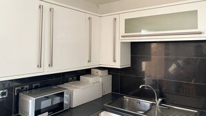 A modern kitchen with white cabinets, a black countertop, a stainless steel sink, and a microwave. - Dagenham - Stay 5 - Garden - Parking - Petfriendly (Dagenham)