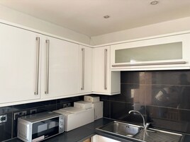 Una cocina moderna con armarios blancos, encimera negra, pileta de acero inoxidable y un microondas.
