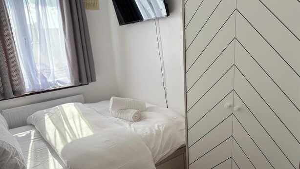 A neatly made bed with white linens, a flat-screen TV mounted on the wall, and a chevron-patterned wall. - Dagenham - Stay 5 - Garden - Parking - Petfriendly (Dagenham)