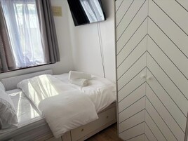 Una cama bien tendida con sábanas blancas, un televisor de pantalla plana montado en la pared y un revestimiento de pared con estampado en zigzag.