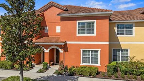A two-story residential building with a red and yellow facade, white window frames, and a tiled roof. - 8893 Candy Palm Road (Kissimmee)