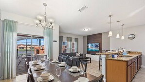 A modern kitchen with a central island, dining area with a set table, and a living room with a sofa and TV. - 8893 Candy Palm Road (Kissimmee)