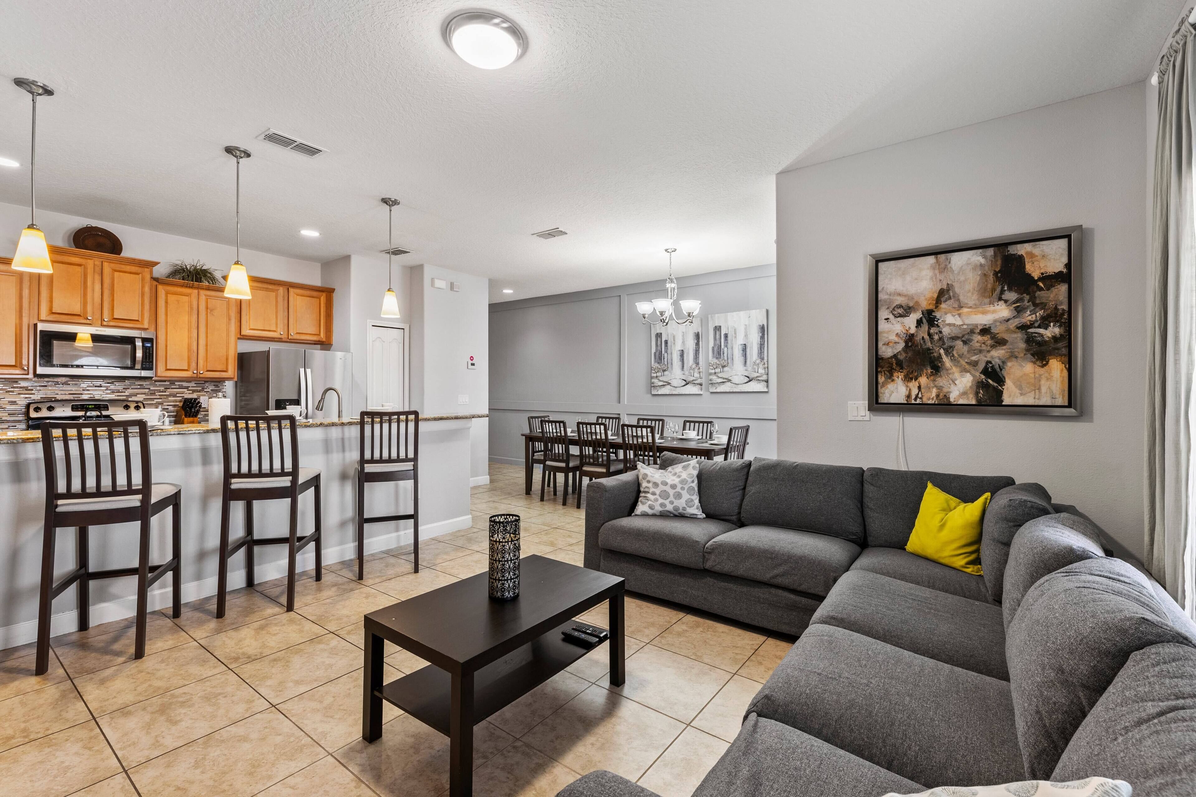 A modern kitchen with wooden cabinets, a central island, and a dining area with a gray sofa and a painting on the wall.