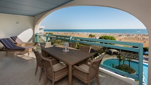 Uma varanda com móveis de vime, piscina e vista para a praia e o oceano.