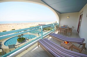 A balcony with a view of a beach and a pool. There are lounge chairs and a table with fruit. - Family fun resort with pool, beach and terrace (Bibione)