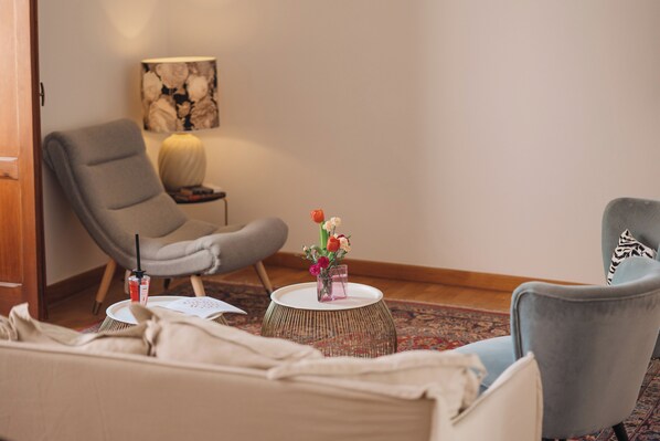 A room with a grey armchair, a blue armchair, a round coffee table with a vase of flowers, a lamp, and a framed picture on the wall. - Loft by Melo - Seaview terrace (Siracusa)