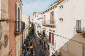 A narrow street with buildings on either side, featuring balconies and a flag. - Loft by Melo - Seaview terrace (Siracusa)