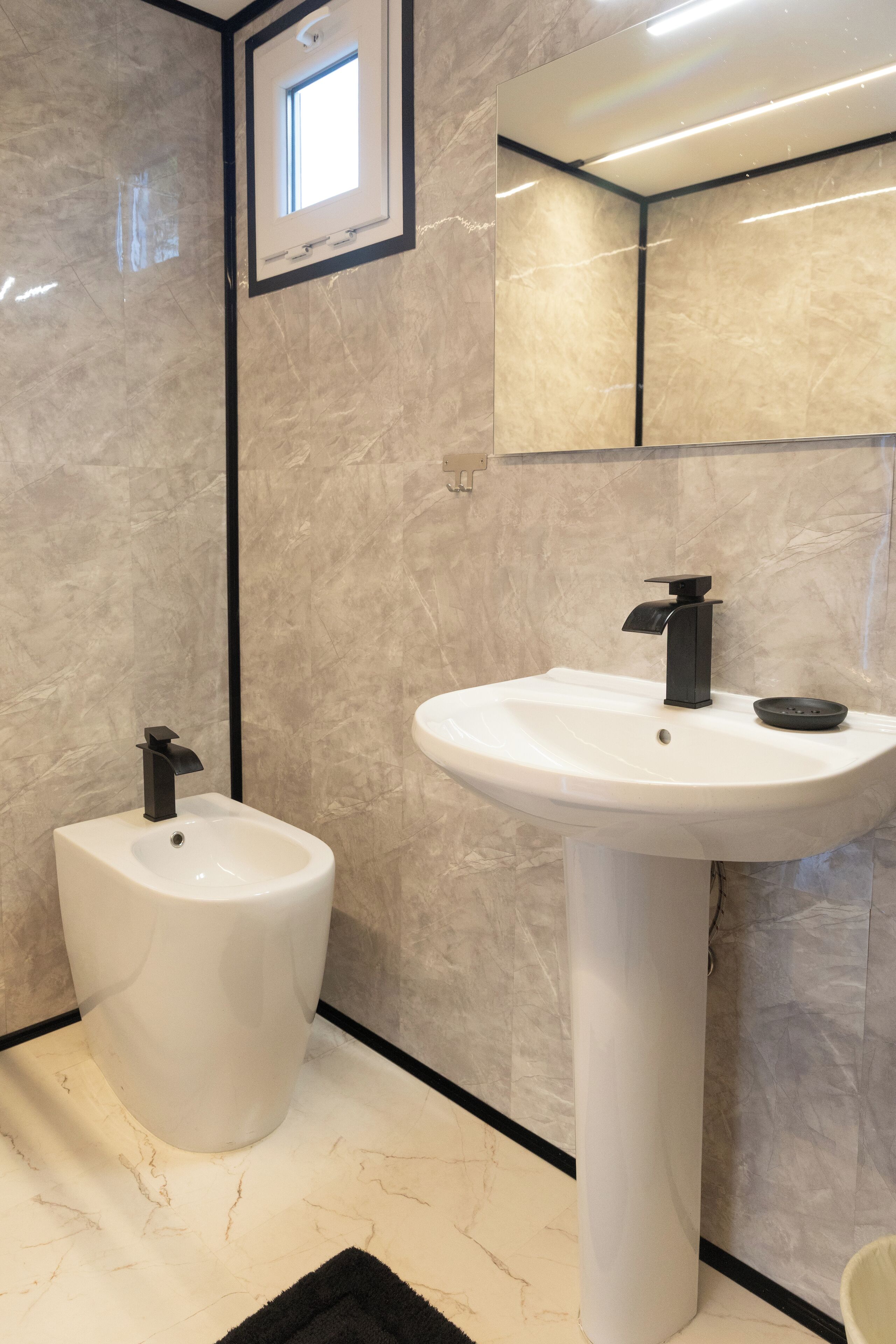 A modern bathroom with a bidet, a pedestal sink, and a large mirror.