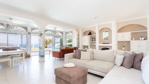 A spacious living area with a large sofa, ottoman, and dining table. There are white cabinets and a chandelier. - 4 bedroom house with pool, garden and beautiful views of the valley and the sea. (Santa Úrsula)