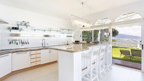 A modern kitchen with white cabinetry, a granite countertop, and a bar area with white stools. - 4 bedroom house with pool, garden and beautiful views of the valley and the sea. (Santa Úrsula)