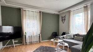 Un salon moderne avec un téléviseur à écran plat, un canapé gris, une table basse et un grand tapis gris.