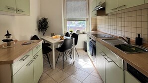 Une cuisine compacte avec des meubles de couleur verte, un plan de travail en bois, une table à manger avec des chaises et un luminaire suspendu.