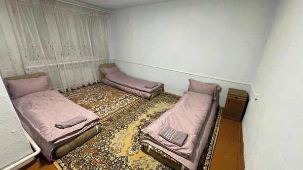 A small room with three single beds, a patterned rug, and a white curtain. - Jakesh (Karakol)
