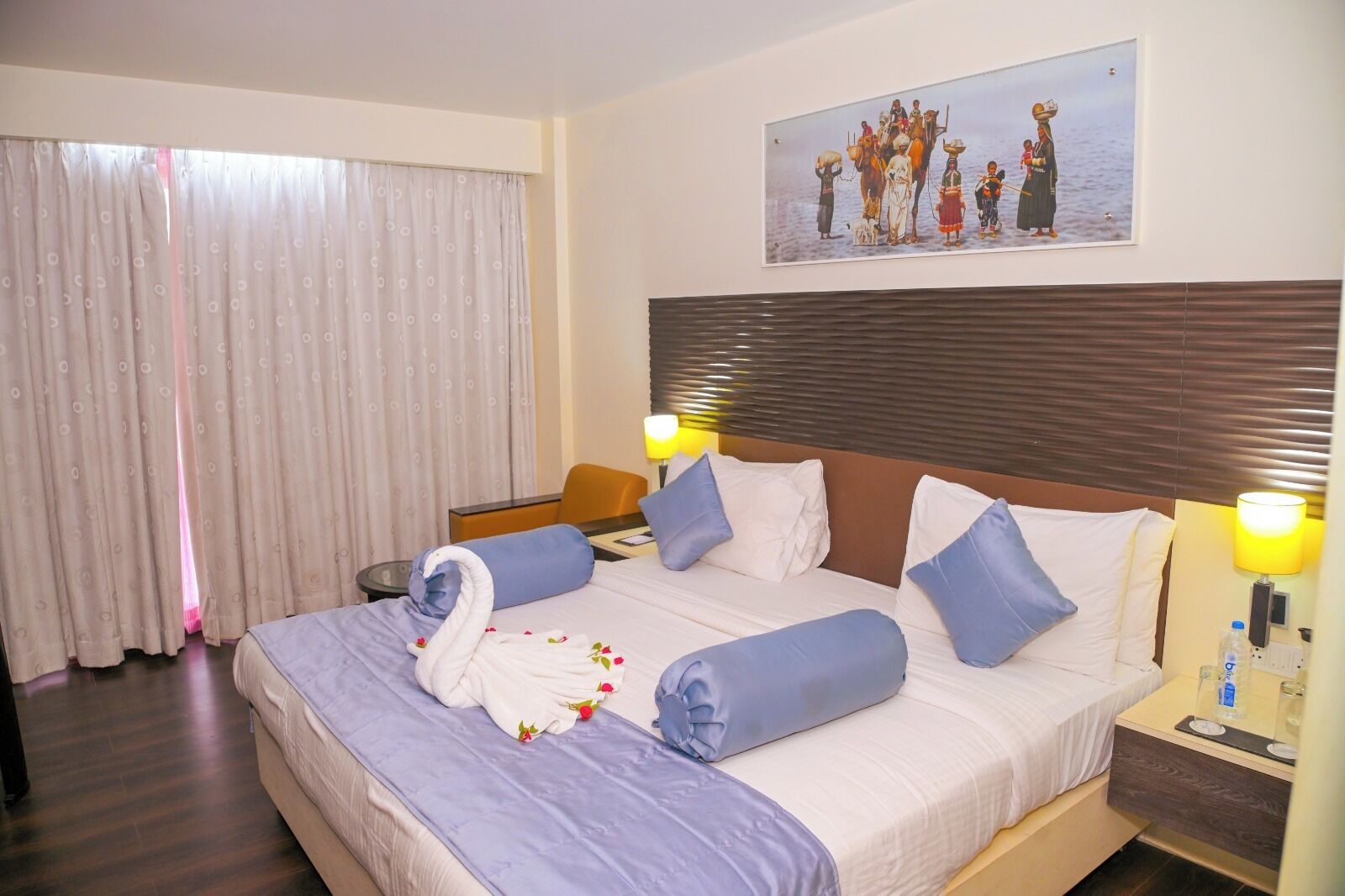 A hotel room with a bed, a headboard, a nightstand, a lamp, a chair, and a window with curtains.