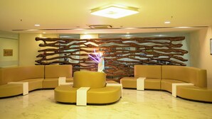 A lobby with a modern design, featuring a central seating area with a unique, abstract wall art and a ceiling light fixture. - Ambar Sarovar Portico (Gandhidham)