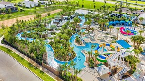 Eine Luftaufnahme eines Resorts mit großem Poolbereich, Wasserrutschen und Palmen.