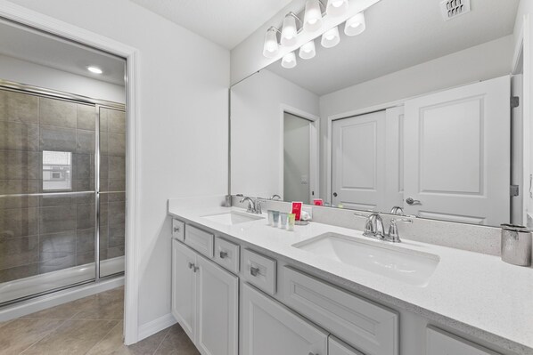 A modern bathroom with a double sink, a large mirror, and a glass shower enclosure. - 16049 Blue Wave Way (Clermont)