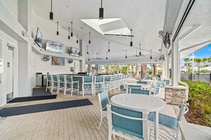 A covered outdoor dining area with white tables and chairs, ceiling fans, and artwork on the walls. - 16049 Blue Wave Way (Clermont)