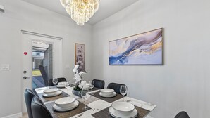 Ein Essbereich mit einem Marmortisch, gedeckt für sechs Personen, schwarzen Stühlen, einer Kristallleuchtreiter und einem großen abstrakten Gemälde an der Wand.