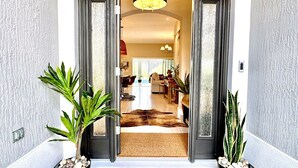 A doorway leading to a living room with a sofa, coffee table, and a lamp. There are two potted plants on either side of the entrance.