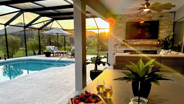A poolside dining area with a table set for two, featuring a fruit platter, glasses, and a jar of seashells.
