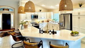A modern kitchen with a large island, white cabinetry, stainless steel appliances, and wicker pendant lights.