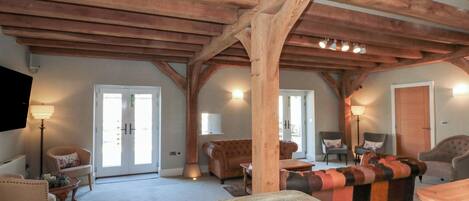A spacious room with a high ceiling supported by wooden beams, a stone fireplace, and a cozy seating area with multiple chairs and a sofa.