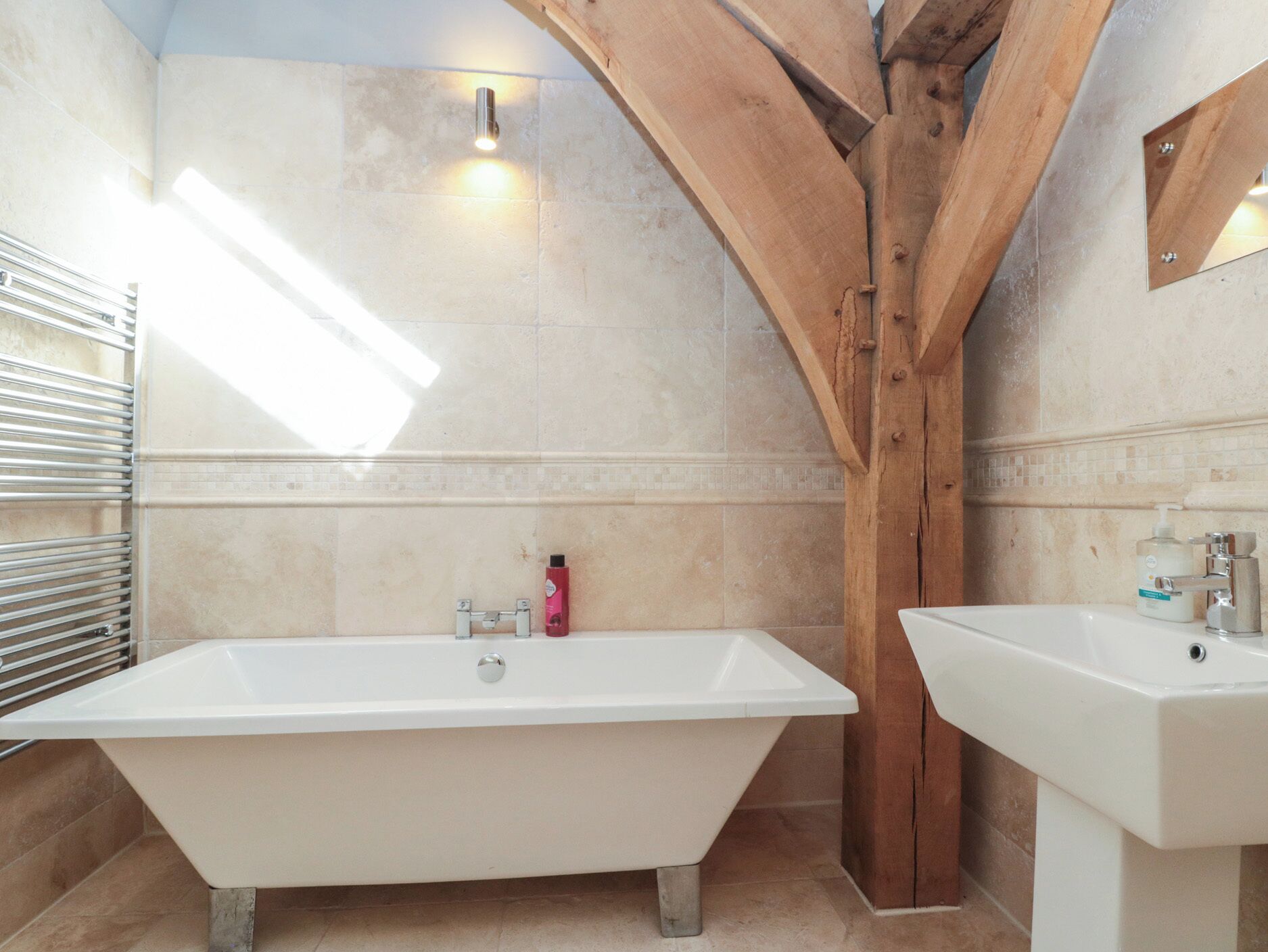 A bathroom with a freestanding bathtub, a sink, and wooden beams.