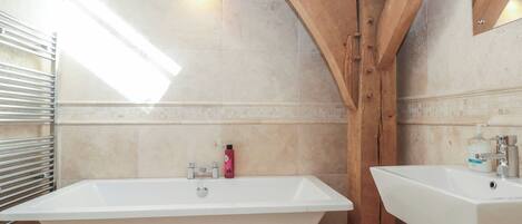 A bathroom with a freestanding bathtub, a sink, and wooden beams.