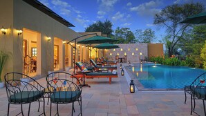 A poolside area with lounge chairs, umbrellas, and a stone wall. - Singhvilas Ranthambore-By Leisure Hotels (Sawai Madhopur)