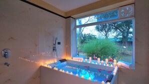 A bathroom with a bathtub, candles, and a window with a view of trees. - Singhvilas Ranthambore-By Leisure Hotels (Sawai Madhopur)