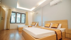 A hotel room with two beds, wooden flooring, a large window with curtains, an air conditioning unit, and a bedside table. - Hoang Lam Hotel (Hai Phong)