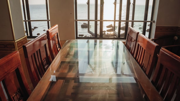 A dining area with a glass table and wooden chairs, overlooking a rocky shoreline with the sea in the background. - Hoang Lam Hotel (Hai Phong)