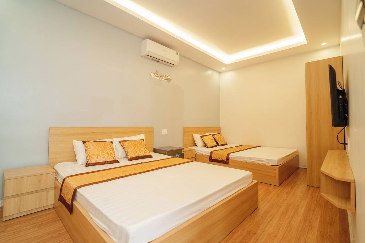 A hotel room with two beds, wooden headboards, a flat-screen TV mounted on the wall, and a built-in air conditioning unit.