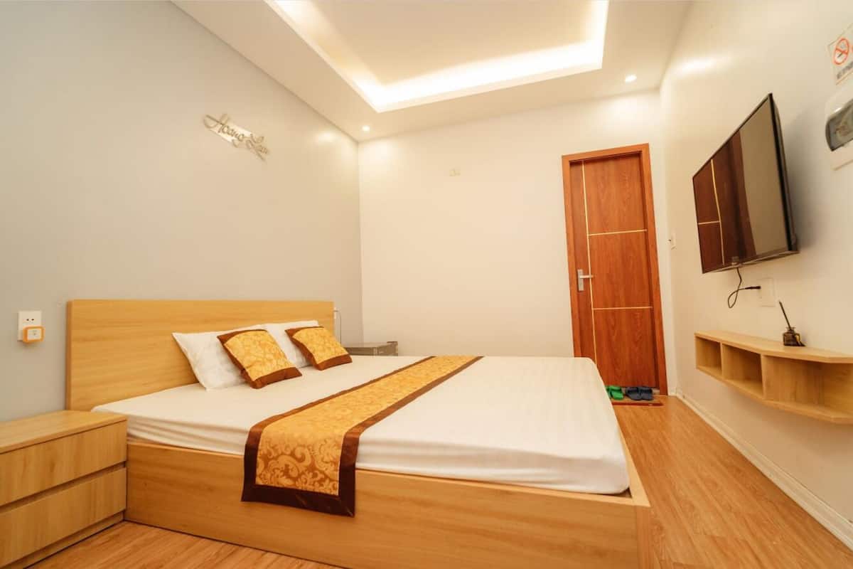 A bedroom with a wooden bed, a nightstand, a TV mounted on the wall, and a wooden door.