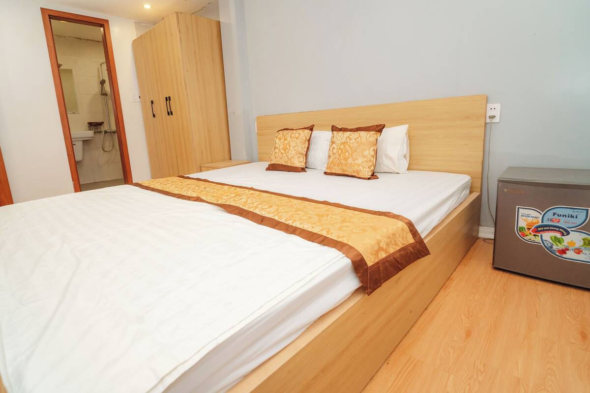 A neatly made bed with a wooden headboard, a bedside table, and a small cabinet.