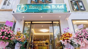 The exterior of Hoang Lam Hotel with a clear entrance, large glass windows, and a signboard displaying the hotel's name and contact information. - Hoang Lam Hotel (Hai Phong)