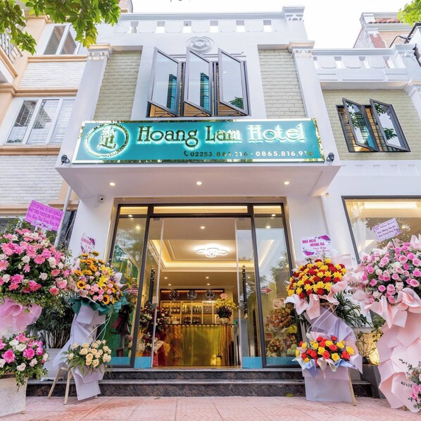 The exterior of Hoang Lam Hotel with a clear entrance, large glass windows, and a signboard displaying the hotel's name and contact information. - Hoang Lam Hotel (Hai Phong)