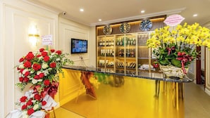 A hotel reception area with a counter, a television, a clock, and a floral arrangement. - Hoang Lam Hotel (Hai Phong)